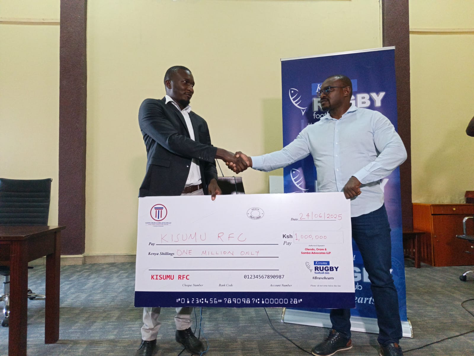 Kisumu RFC chairman Dr Gabriel Ouma receives a dummy cheque from KRU Honorary Secretary Ray Olendo. PHOTO/Brian Mwenje